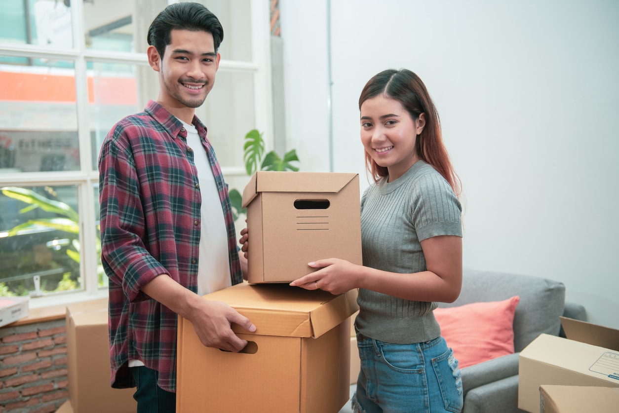 Young Asian couple packing their belongings into cardboard boxes before or after moving to new residence.