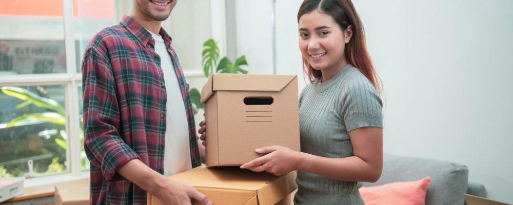 Young Asian couple packing their belongings into cardboard boxes before or after moving to new residence.